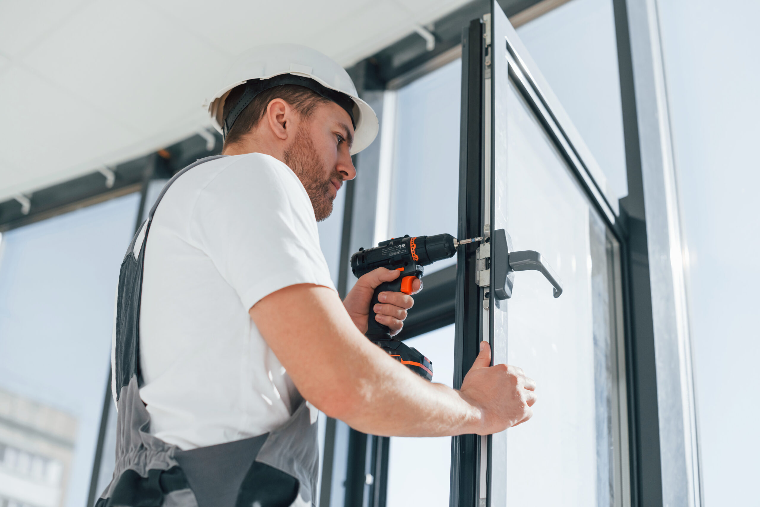 In grey uniform. Repairman is working indoors in the modern room.