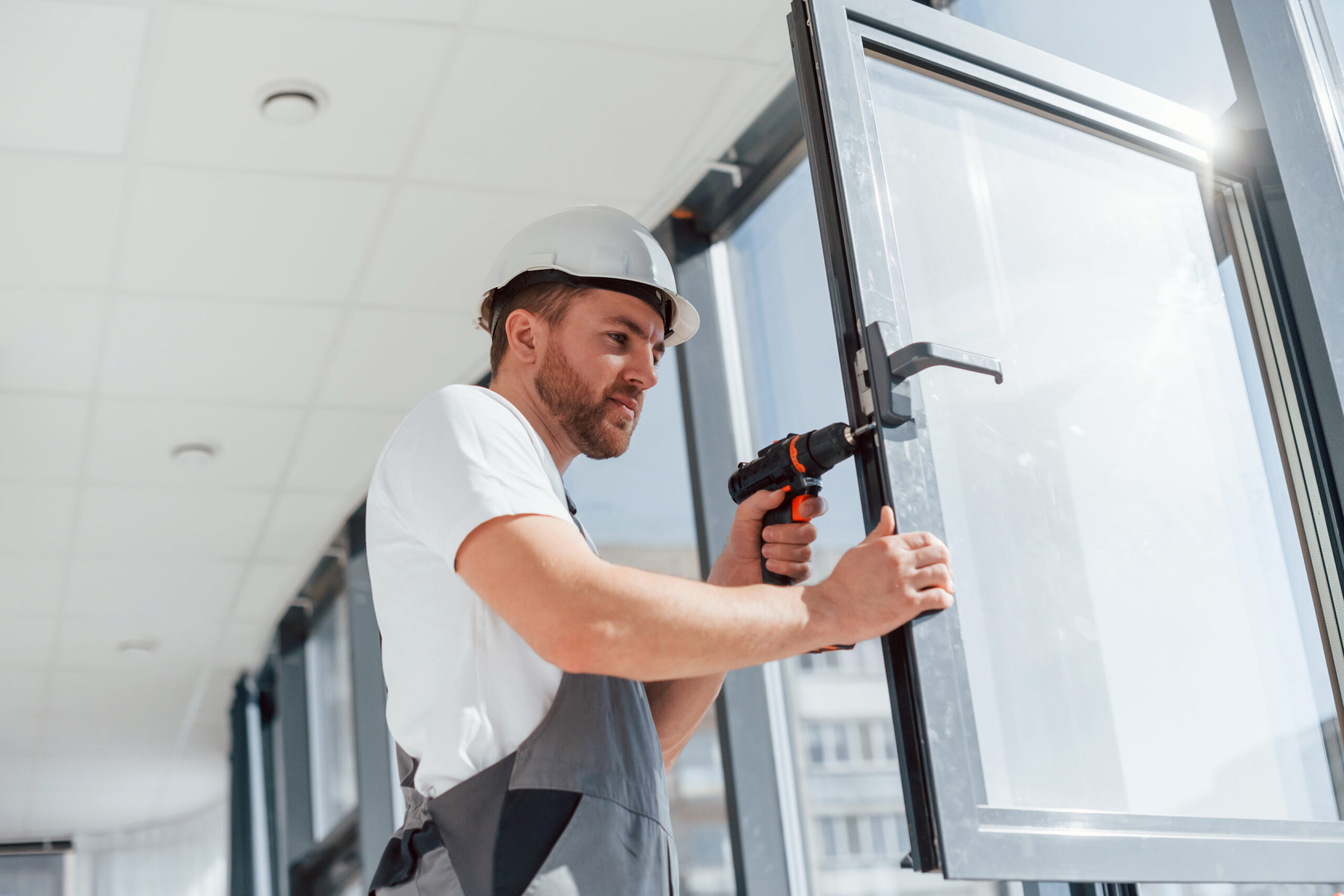 In grey uniform. Repairman is working indoors in the modern room.