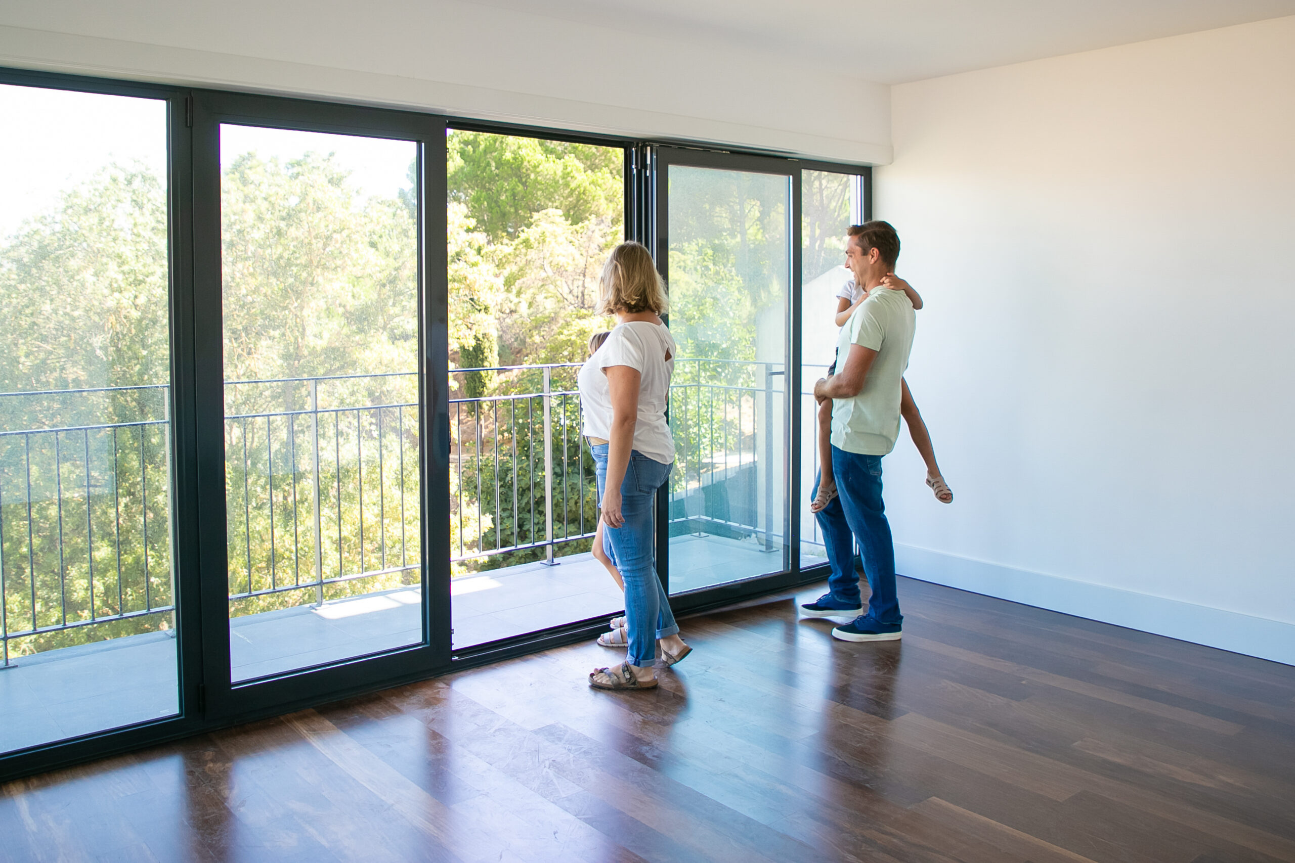 Happy family with kids looking at balcony and smiling. Back view of blonde mother. Daughter sitting on father hands. People watching new house or flat. Mortgage, relocation and moving day concept